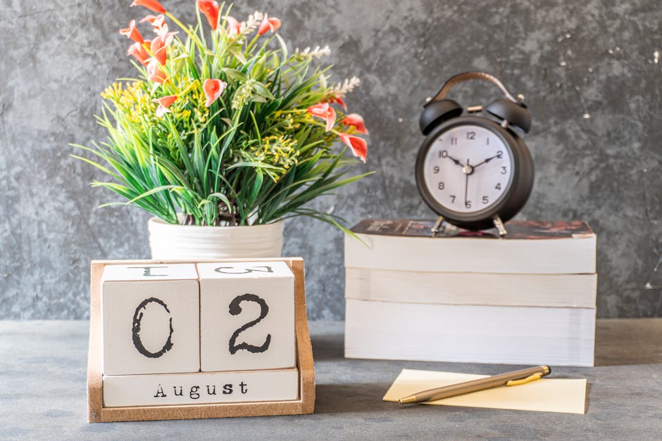 Close-up of a calendar set to August 2nd with a clock, flower vase, and writing pad on a desk.