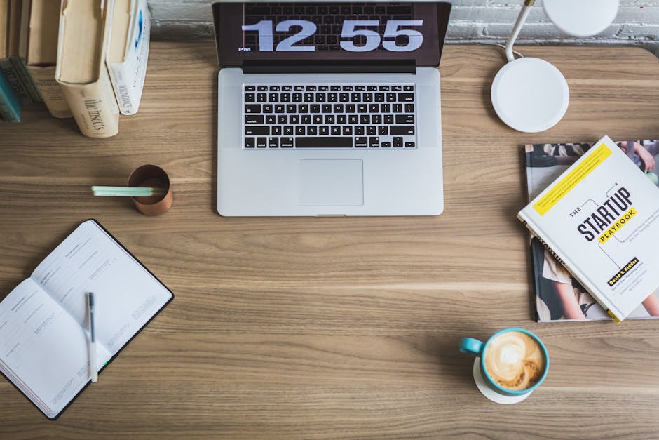 Flat lay of a modern workspace with a laptop, coffee cup, and startup books on a wooden desk.